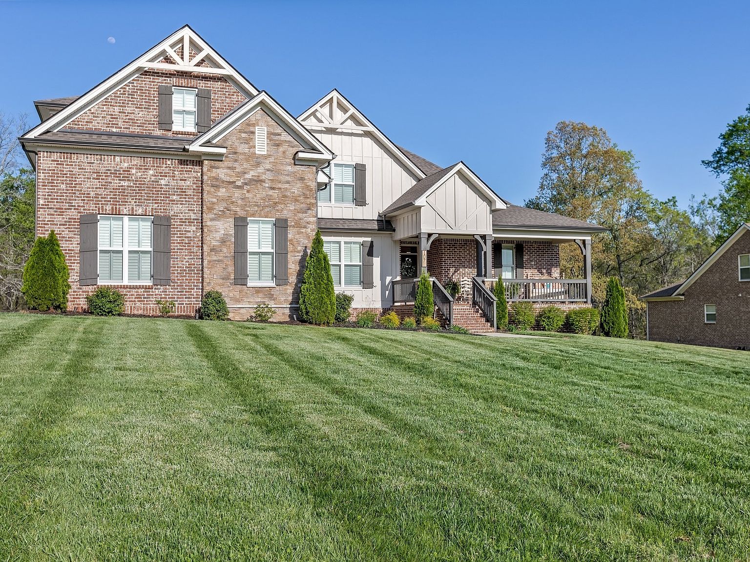 Three-quarter view of 1070 Hideaway Road showing the full brick craftsman elevation, twin gables, board-and-batten accents, and the green lawn that runs to the property line