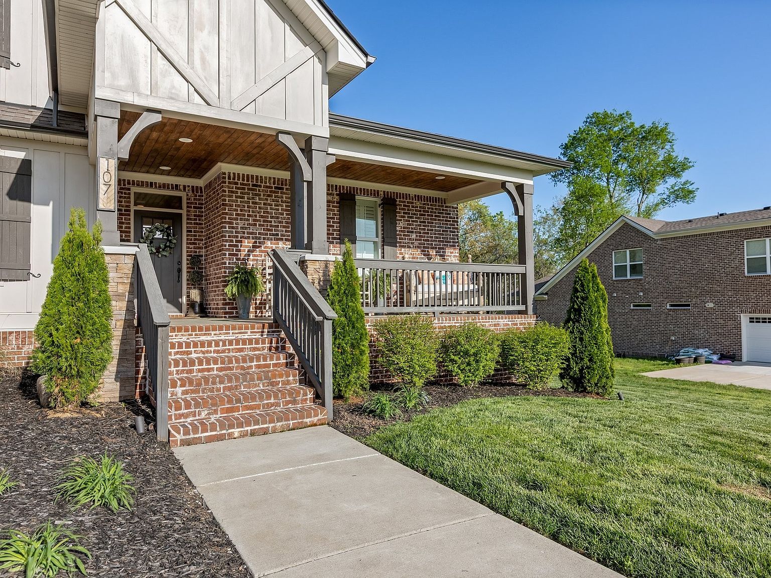 Approach to the front porch of 1070 Hideaway Road from the side path, with stone steps, black metal handrail, and a long covered porch extending the length of the brick facade