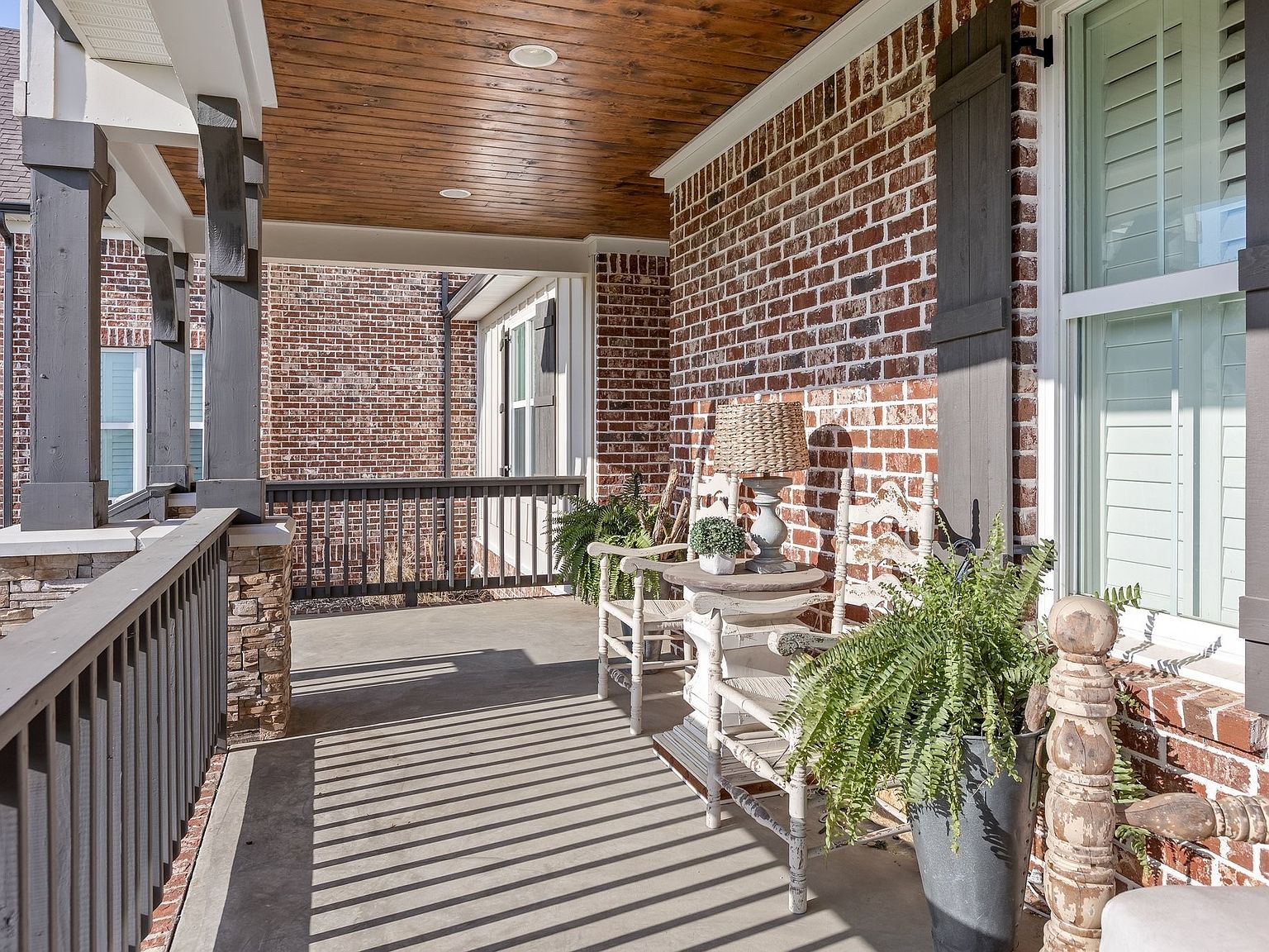 Long perspective view down the front porch of 1070 Hideaway Road showing brick columns, wicker furniture, planters, and the wood plank ceiling extending the length of the home